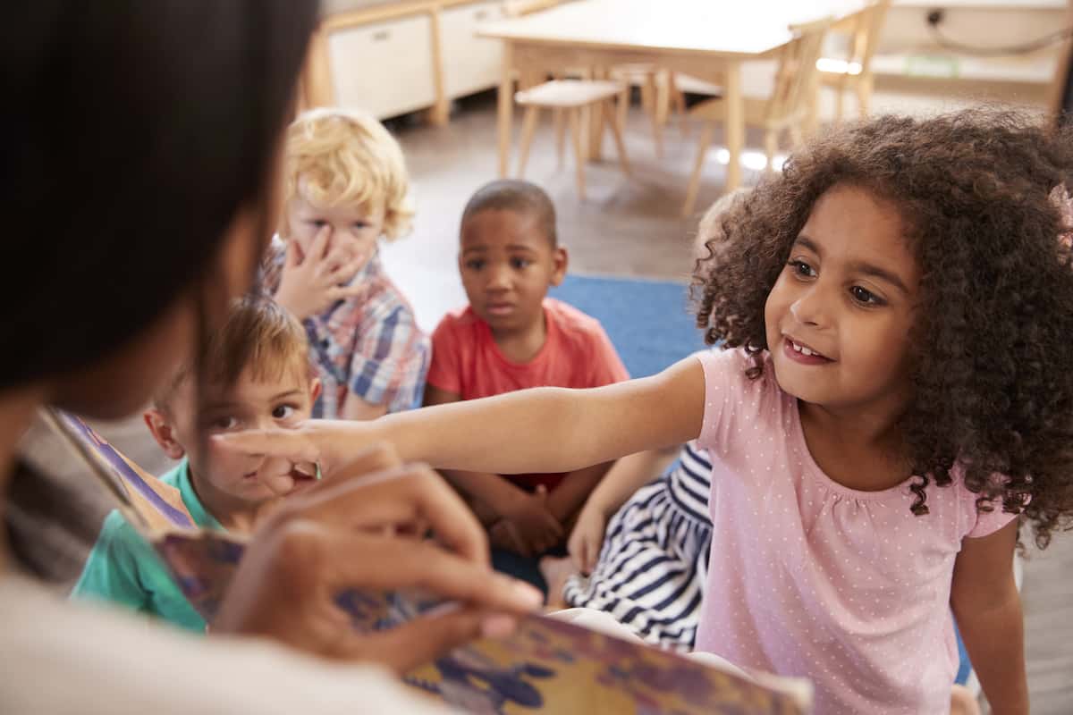 Pupils At Montessori School Looking At Book With Teacher